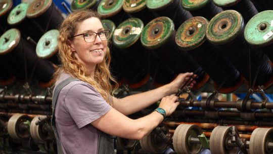 a white female with long, curly, strawberry blonde hair, standing in front of a large mill machine