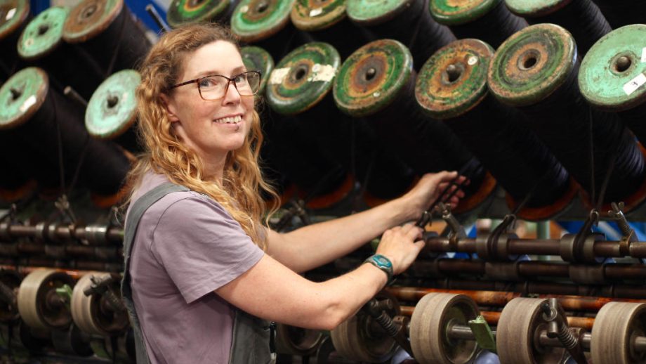 a white female with long, curly, strawberry blonde hair, standing in front of a large mill machine