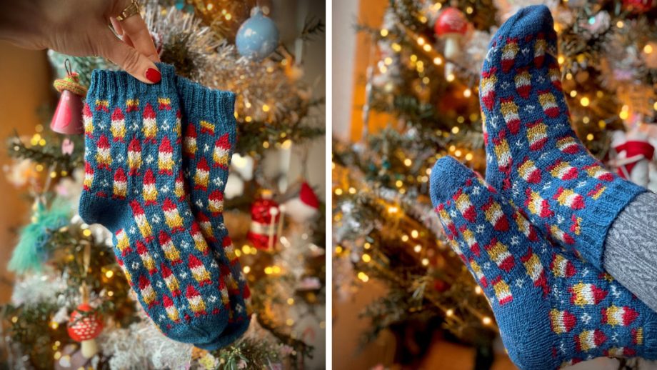 Blue socks with all-over gnome pattern. In the background of the photo is the warm glow of Christmas tree lights.