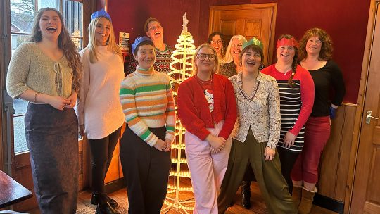 The mill folk gathering around a Christmas tree, grinning.